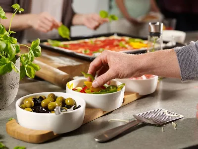 On a counter there are several small white bowls of olives and vegetables, with a Kensington Fromage cheese grater in front of them.