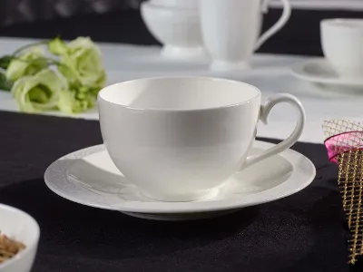 White porcelain cup and saucer on a black tablecloth, with blurred white cups in the background and a decorative flower.