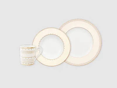 Eine weiße Tasse und zwei weiße Teller mit Goldrand sind vor einem schlichten hellen Hintergrund angeordnet.