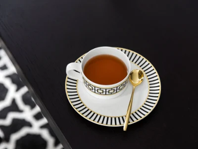 A MetroChic teacup with a golden spoon on a matching saucer, placed, on a dark wooden table.