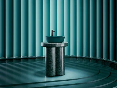 The round Artis countertop washbasin in the color Teal stands on a marble base in the same color, surrounded by blue-green tones. A soft, diffused light and the rounded steps at the foot of the base, which lead into a water area, create a calm, almost meditative atmosphere.