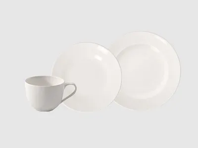 Eine weiße Tasse und zwei weiße Teller werden vor einem schlichten hellen Hintergrund präsentiert.