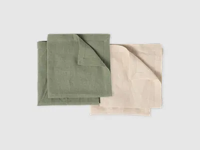 Zwei gefaltete Stoffservietten, eine grüne und eine beige, nebeneinander auf einem schlichten Hintergrund.