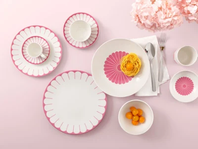 Table setting with Villeroy & Boch Fleur Cassis plates, pasta, clementines, and flowers on a pink background.