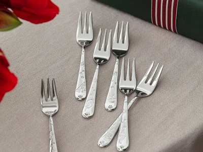 Six silver dessert forks are arranged on a beige tablecloth next to a green gift box with red and white striped ribbon.
