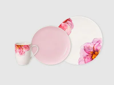 Eine Tasse, ein Teller und ein Essteller aus Keramik mit rosa Blumenmustern und einem soliden hellrosa Finish auf hellem Hintergrund.