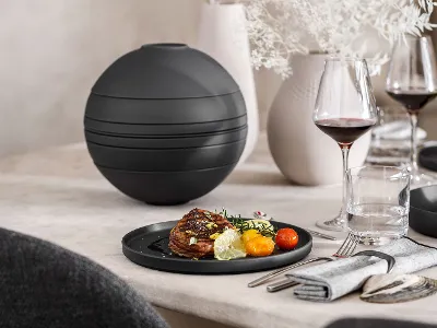 A fully assembled black La Boule beside a single plate with food on top.