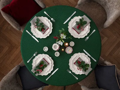Widziany z góry okrągły stół dla czterech osób z białymi talerzami Toy's Delight Royal Classic Villeroy & Boch, zielonym obrusem i świątecznymi dekoracjami, w tym liśćmi ostrokrzewu, jagodami i laskami cukrowymi.