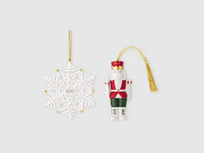 Ein weißes Schneeflockenornament und ein Nussknackerornament mit goldenen hängenden Schnüren vor einem schlichten Hintergrund.