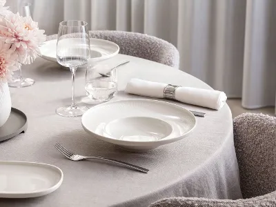 Table élégante dressée avec assiettes creuses en porcelaine Afina, verres à vin blanc et à eau assortis. Une atmosphère lumineuse avec un style de repas moderne et sophistiqué.