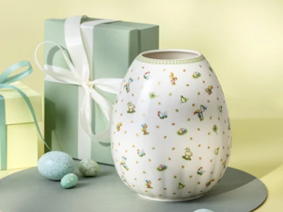 A white Easter Delight vase with floral designs A white Easter Delight vase with floral designs is displayed beside two pastel gift boxes and speckled eggs.