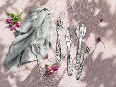 Ein Besteckset und eine graue Stoffserviette sind auf einer rosa strukturierten Oberfläche mit verstreuten Blumen angeordnet.