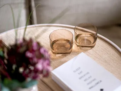 Two orange Like glasses on a wooden table next to a bouquet of flowers and a book.