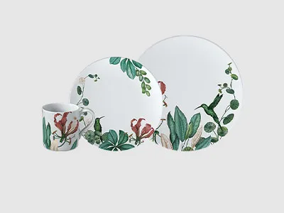 Weißes Keramikgeschirrset mit grünen Blättern und roten Vogelmotiven, bestehend aus einer Tasse, einem kleinen und einem großen Teller.
