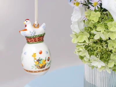 Ceramic Annual Easter Edition 2026 ornament with a chicken Ceramic Annual Easter Edition 2026 ornament with a chicken design hanging near a bouquet of green and white flowers in a vase.
