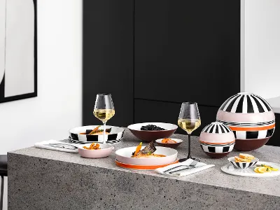 Ein moderner Tisch mit gemustertem La Boule und der gemusterten La petite Boule, Weingläsern und Snacks auf einer grauen Arbeitsplatte in einer minimalistischen Küche.