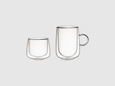 Abgebildet sind zwei klare, doppelwandige Glasbecher, einer mit Henkel und einer ohne, auf schlichtem hellem Untergrund.