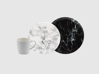 Eine weiße Tasse, ein weißer Teller mit Marmormuster und ein schwarzer Teller mit Marmormuster auf schlichtem Hintergrund.
