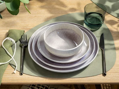 Perlemor Sand & Like Sage – Soft Natural Tones in Perfect Balance Vue du dessus d’un couvert individuel avec la collection Perlemor Sand de Villeroy & Boch : assiettes superposées et bol à céréales dans des tons beiges chaleureux avec un émail artisanal, accompagnés d’un verre à eau Like Sage. L’arrangement dégage une élégance naturelle et apaisante, parfaite pour des repas modernes et décontractés.