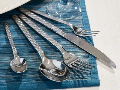 Silver Montauk cutlery set arranged on a blue woven placemat next to a white plate and a glass.