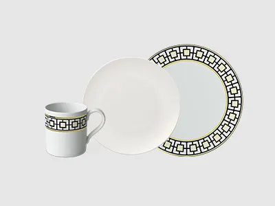 Eine Tasse, eine Schüssel und ein Teller sind mit einem schwarzen geometrischen Randmuster auf hellgrauem Hintergrund.