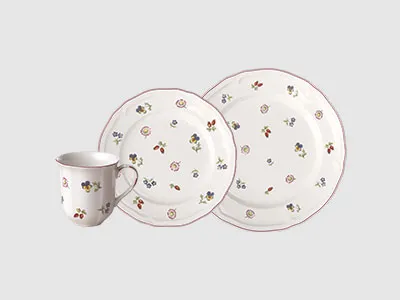 Eine weiße Tasse und zwei Teller, alle mit kleinen, verstreuten Blumenmustern auf hellem Hintergrund.