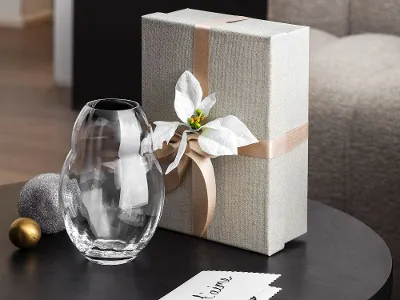 A table with a wrapped gift box, adorned with a white bow and a decorative Rose Garden Home glass vase