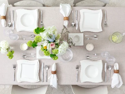 Vue du dessus d’une table minimaliste avec assiettes en porcelaine NewWave, tasse à café et soucoupe, verrerie Boston et Boston Green, et couverts NewWave et Blacksmith. Des vases de fleurs ajoutent une touche naturelle et élégante à la composition épurée.
