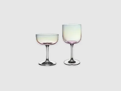 Zwei Stielgläser aus klarem Glas, ein Coupe- und ein Weinglas, stehen nebeneinander auf einem schlichten hellen Hintergrund.