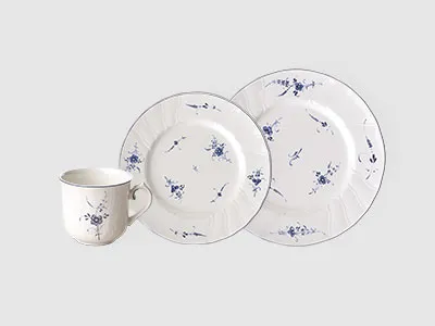 Eine weiße Keramiktasse und zwei Teller mit blauen Blumenmustern sind vor einem schlichten hellgrauen Hintergrund angeordnet.