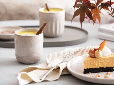 Boho-inspiriertes Tischgedeck mit Villeroy & Boch Perlemor Sand Teller und Becher, serviert mit feinem Gebäck und Heißgetränk auf Holztisch.