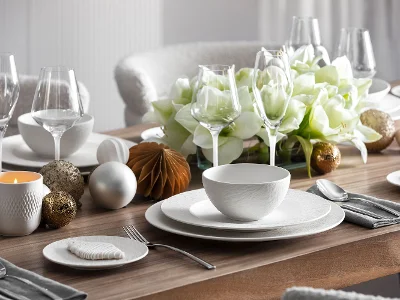 Une table élégante dressée avec la vaisselle Manufacture, la verrerie, l'argenterie, ainsi qu'un centre de table composé de fleurs blanches et d'ornements décoratifs.