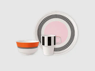 Ein Teller, eine Schüssel und eine Tasse mit geometrischen Mustern in Schwarz, Weiß, Rosa und Orange sind zusammen angeordnet.