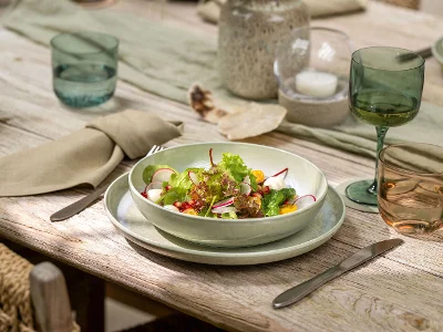 Un saladier trône sur une table dressée avec des verres, des assiettes et des serviettes beiges Perlemor.