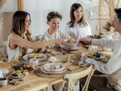 Family of four enjoying a festive meal at a Christmas table set with Perlemor plates and Winter Glow glasses, with the mother serving a child.