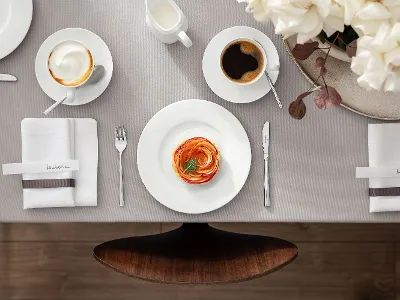 A beautiful dining table setting with the Villeroy & Boch Royal collection, including a plate with food, a coffee cup, a cappuccino, cutlery, napkins and a jug of milk. There is also a flower arrangement on the right-hand side of the table.