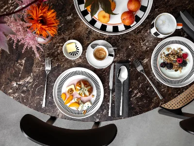 Vue de dessus d'une table en marbre avec des bols de fruits, de café, de céréales et de yaourt de la collection Memphis de Villeroy & Boch, des couverts et des décorations florales.