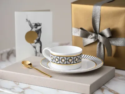 A golden MetroChic tea cup and saucer on a marble table.