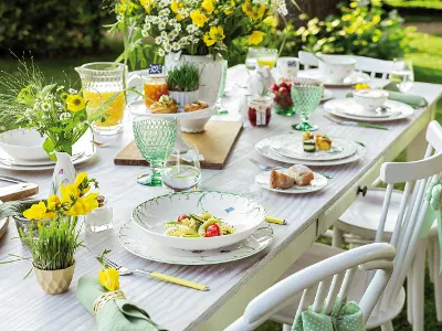 An elegantly set outdoor dining table with Colourful Spring crockery with a spring theme, decorated with fresh flowers and ready for a meal in the garden.