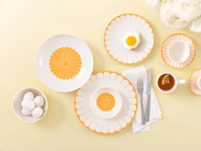 Table setting with Villeroy & Boch Fleur Soleil plates, eggs, tea with a slice of lemon, and white flowers on a light yellow background.