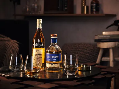 Zwei Flaschen Scotch Whisky und drei Gläser von Villeroy & Boch stehen auf einem Holztisch. Im Hintergrund sind Bücher und eine Dekofigur zu sehen.