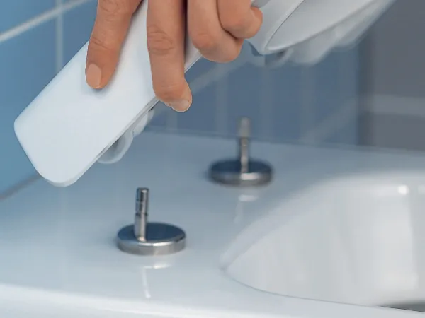 Una mano rimuove il copriwater in un bagno con pareti piastrellate blu.