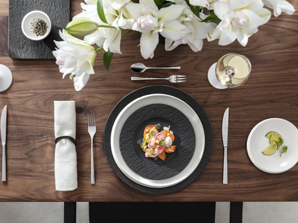 Elegant table setting with a seafood dish on Manufacture plates, white flowers, a glass of white wine and a small plate with lemon slices.
