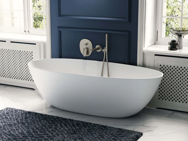 Biała wanna Antao na tle niebieskiej ściany. Nowoczesna łazienka z białą wanną wolnostojącą, niebieską ścianą akcentującą i marmurową podłogą. Naturalne światło wpada przez pobliskie okna.