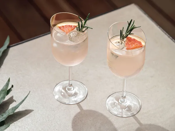 Due bicchieri da vino rosso NewMoon con cocktail al rosmarino e pompelmo su un tavolo di legno.
