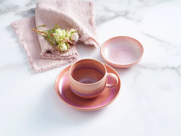 aus-perlemorcoral-indoor-nofood-nopeople-giftset7081 The 5pcs Perlemor Coffee Set in pink, featuring a cup with saucer and a small bowl on the side, is paired with a pink linen napkin atop a marble table.