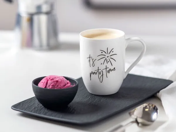 A Statement cup with the words "It's Party Time" on a tray next to a small black bowl of ice cream. 