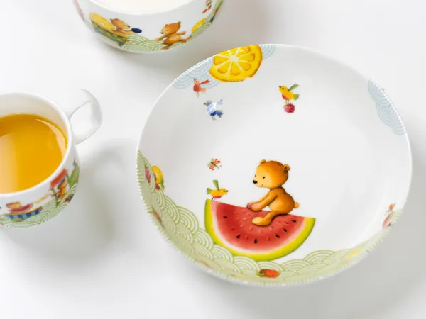 De la vaisselle pour enfants Hungry as a bear avec du jus d’orange Un ensemble de vaisselle pour enfants Hungry as a bear comprenant une assiette, une tasse et un plat creux ainsi que du jus d’orange.