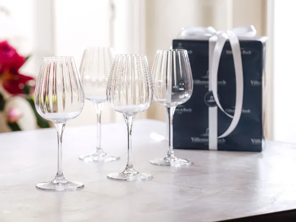 Four crystal wine glasses on a table next to a wrapped gift box with a white ribbon. Four crystal wine glasses on a table next to a wrapped gift box with a white ribbon.