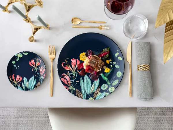 An elegant dining table with Avarua plates and gourmet food, accompanied by gold MetroChic cutlery and a glass of red wine.